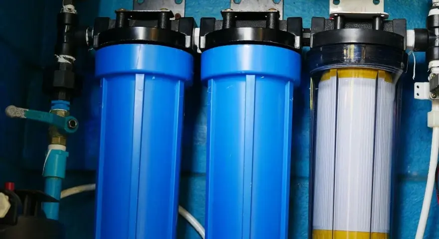 System filtrów do wody, który oczyszcza wodę. Dwa niebieskie filtry i jeden przezroczysty z białym wkładem.