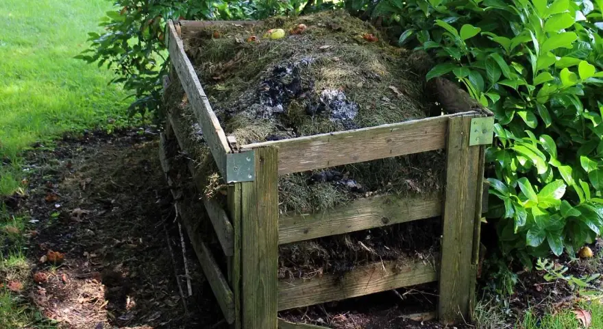 Drewniany kompostownik wypełniony trawą, liśćmi i resztkami organicznymi. To idealne miejsce na odpady zielone, kod odpadu 20 02 01.