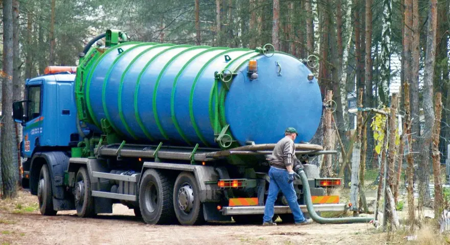 Pracownik podłącza wąż do beczkowozu w celu wywozu osadu z oczyszczalni przydomowej. Przepisy dotyczące takich działań są kluczowe.