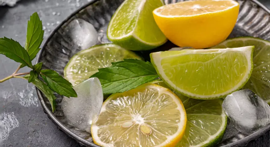 Plasterki cytryny i limonki, kostki lodu i listki mięty na metalowej tacy. Orzeźwiający zapach cytrusów, w tym limonen, unosi się w powietrzu.