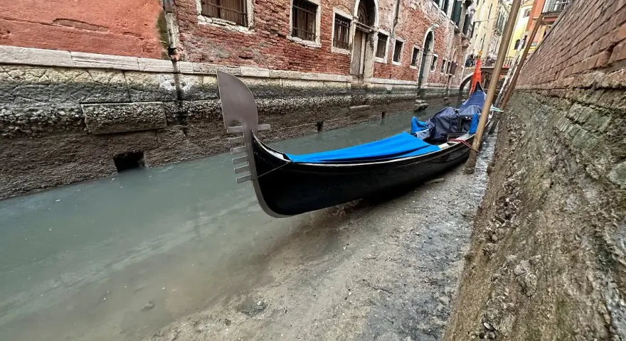Wąski kanał w Wenecji, gdzie widać, jak są odprowadzane ścieki. Przy brzegu zacumowana gondola.