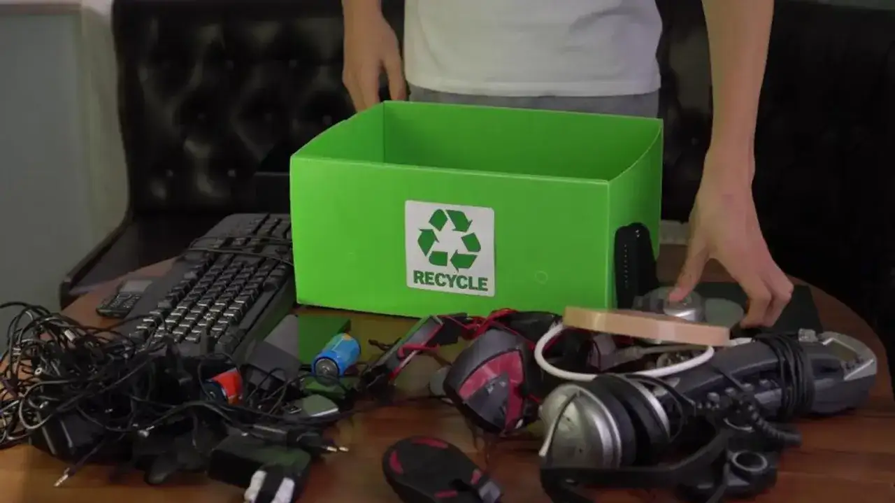 Zbiórka elektrośmieci: klawiatura, myszki, słuchawki, baterie i ładowarki czekają na recykling w zielonym pudełku.