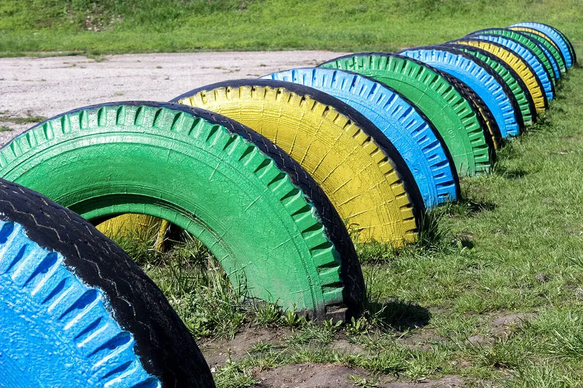 Kolorowe, stare opony ułożone w rzędzie na trawie. Świetny pomysł, co zrobić ze starymi oponami, tworząc kolorową ozdobę lub plac zabaw.