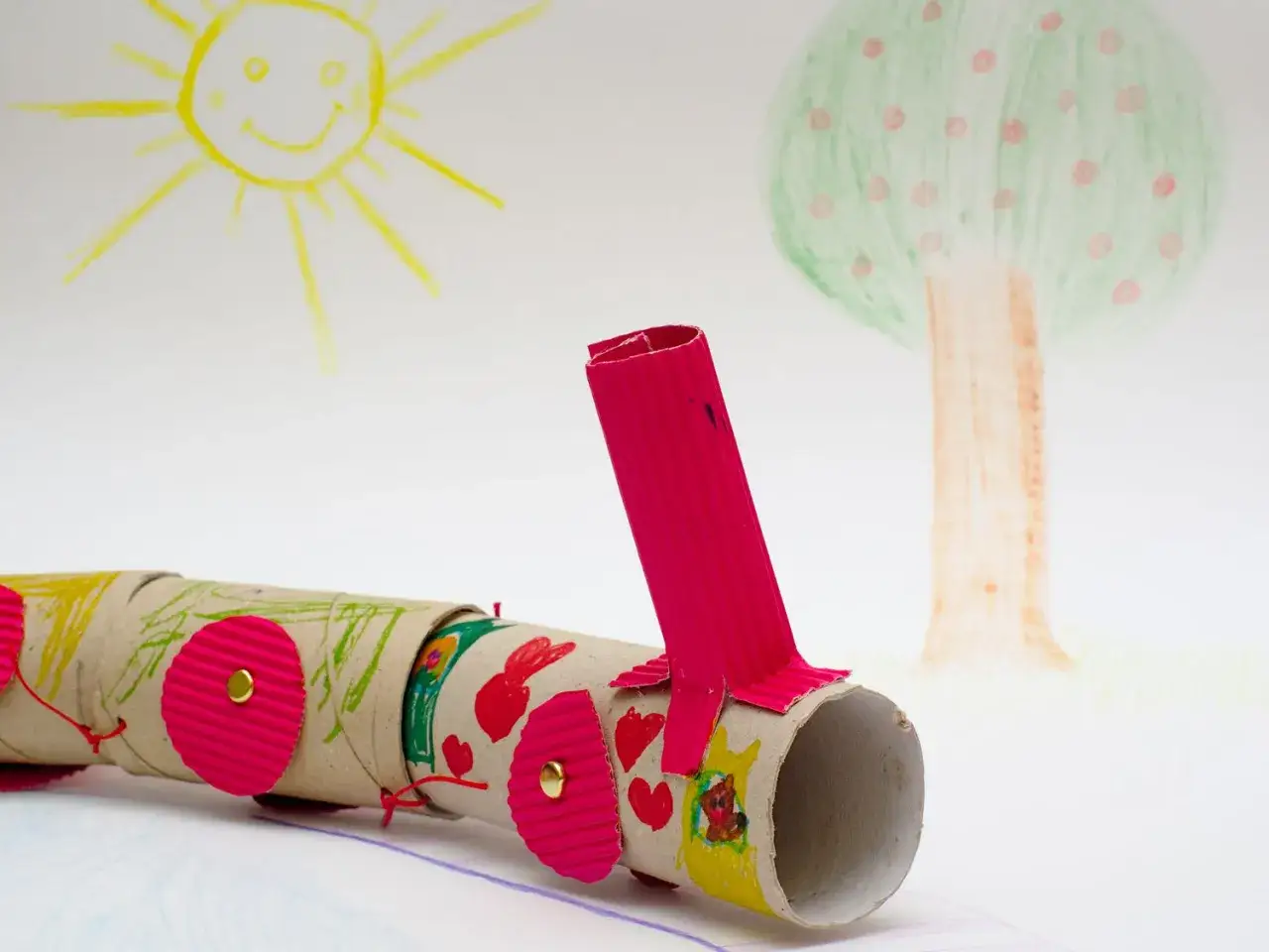 Kolorowy pociąg z rolek papierowych, wesołe zabawki z recyklingu, na tle rysunków słońca i drzewa.