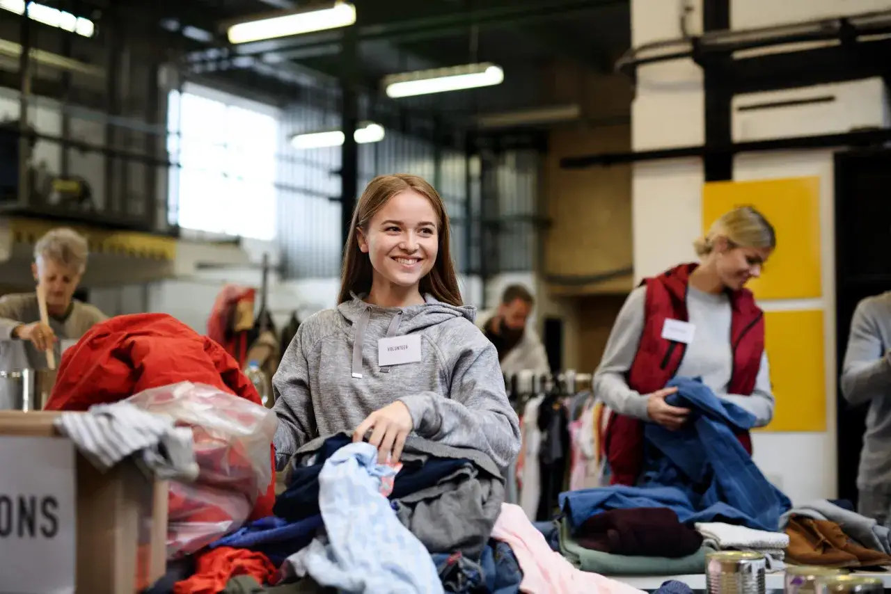 Uśmiechnięta wolontariuszka sortuje ubrania, wspierając akcję recyklingu tekstyliów.
