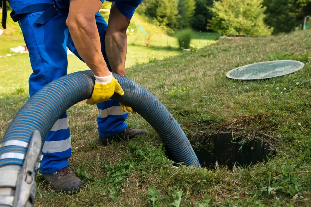 Pracownik w niebieskim kombinezonie podłącza wąż do szamba. Sprawdź wywóz szamba cennik i zadbaj o czystość.