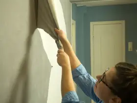 Osoba zdejmuje starą tapetę ze ściany. Zastanawiasz się, gdzie wyrzucić tapetę? Najlepiej do odpadów budowlanych.