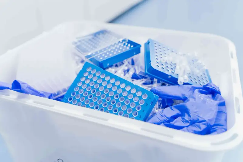 Niebieskie płytki do pipetowania i rękawiczki w pojemniku na odpady laboratoryjne. Kod odpadu 16 03 04.